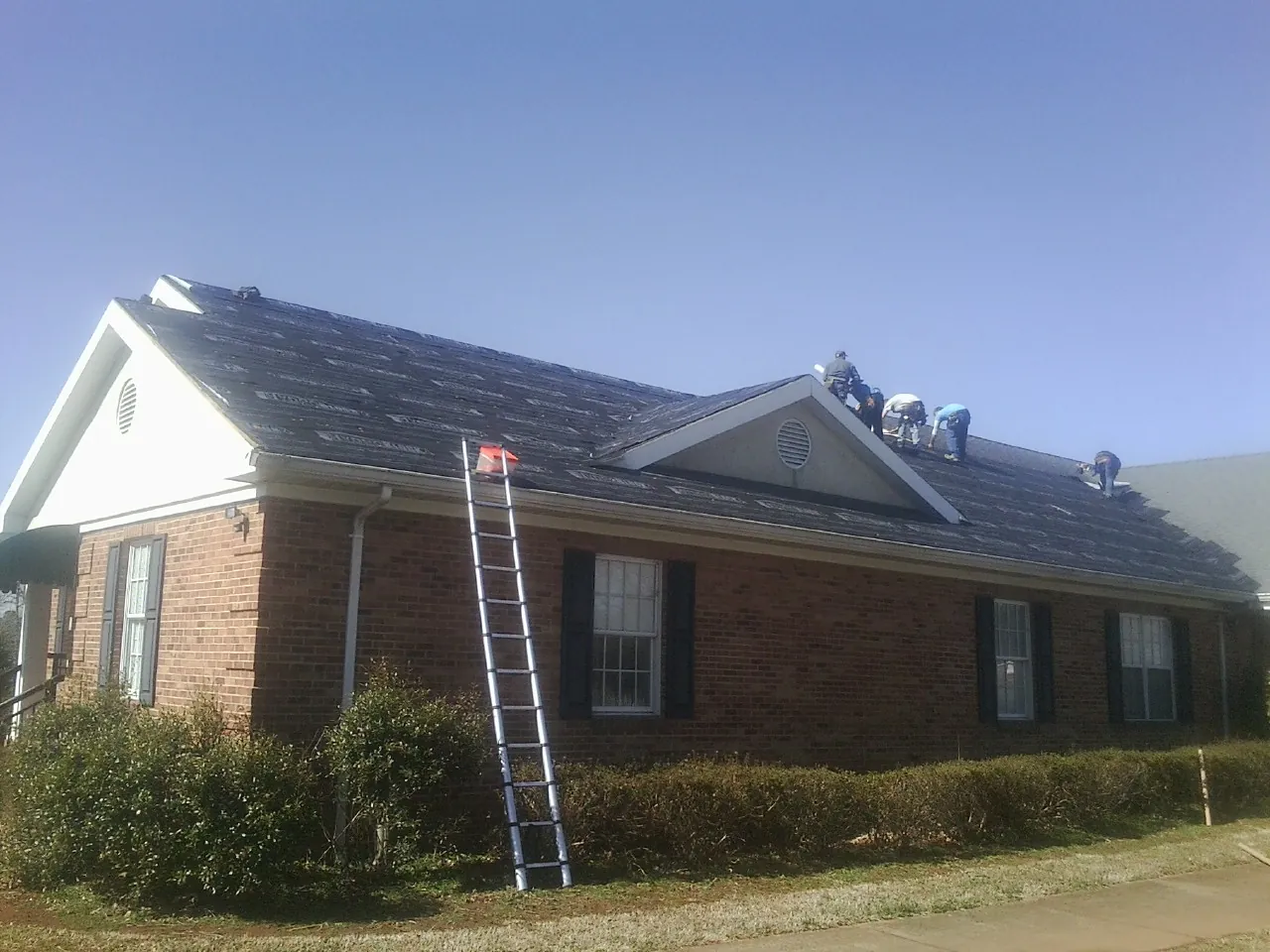 Crew tearing shingles off a brick ranch roof with a ladder set — Emergency Roof Repair work by our crew in Massillon