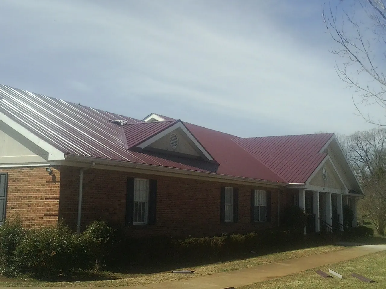 Red metal roof with gabled entries on a long brick building, from a Hail Damage Roof Repair job in Massillon