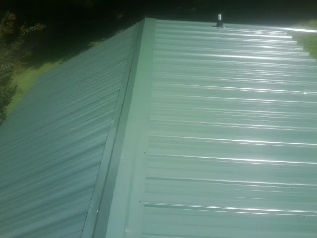 New green metal panels meeting at the ridge of a roof — Flat Roof Repair work by our crew in Massillon