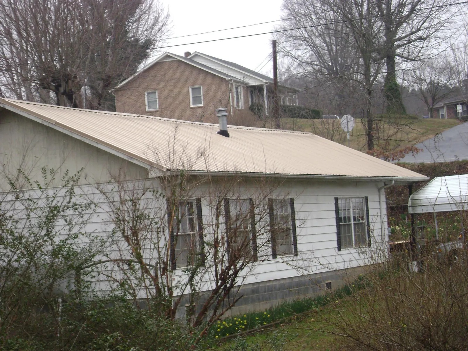 Tan metal roof on a white sided house set into a hillside — Commercial Roofing by Roofing Brothers in Massillon